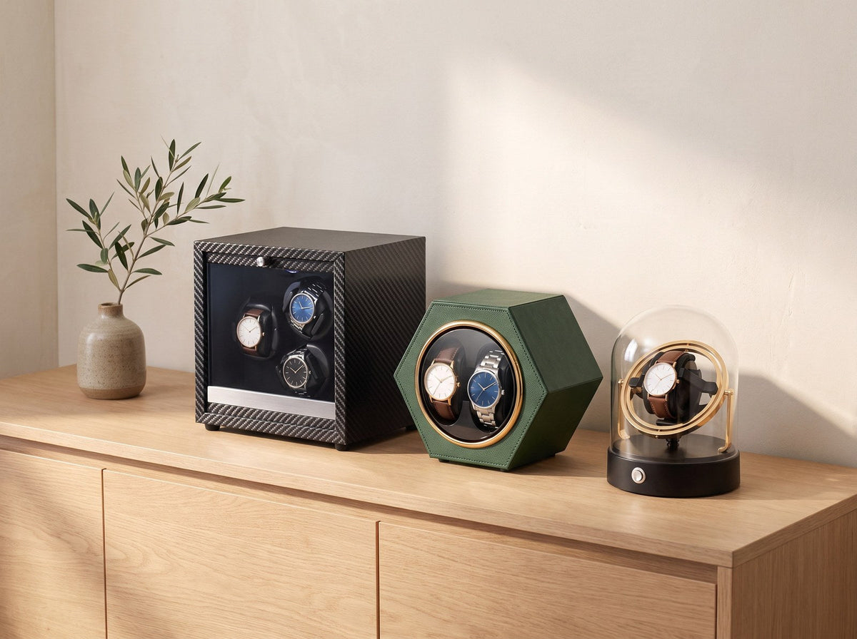 Trois remontoirs automatiques côte à côte : Galerie carbone, Alvéole vert et Orbite doré sous cloche, sur un meuble en chêne Image