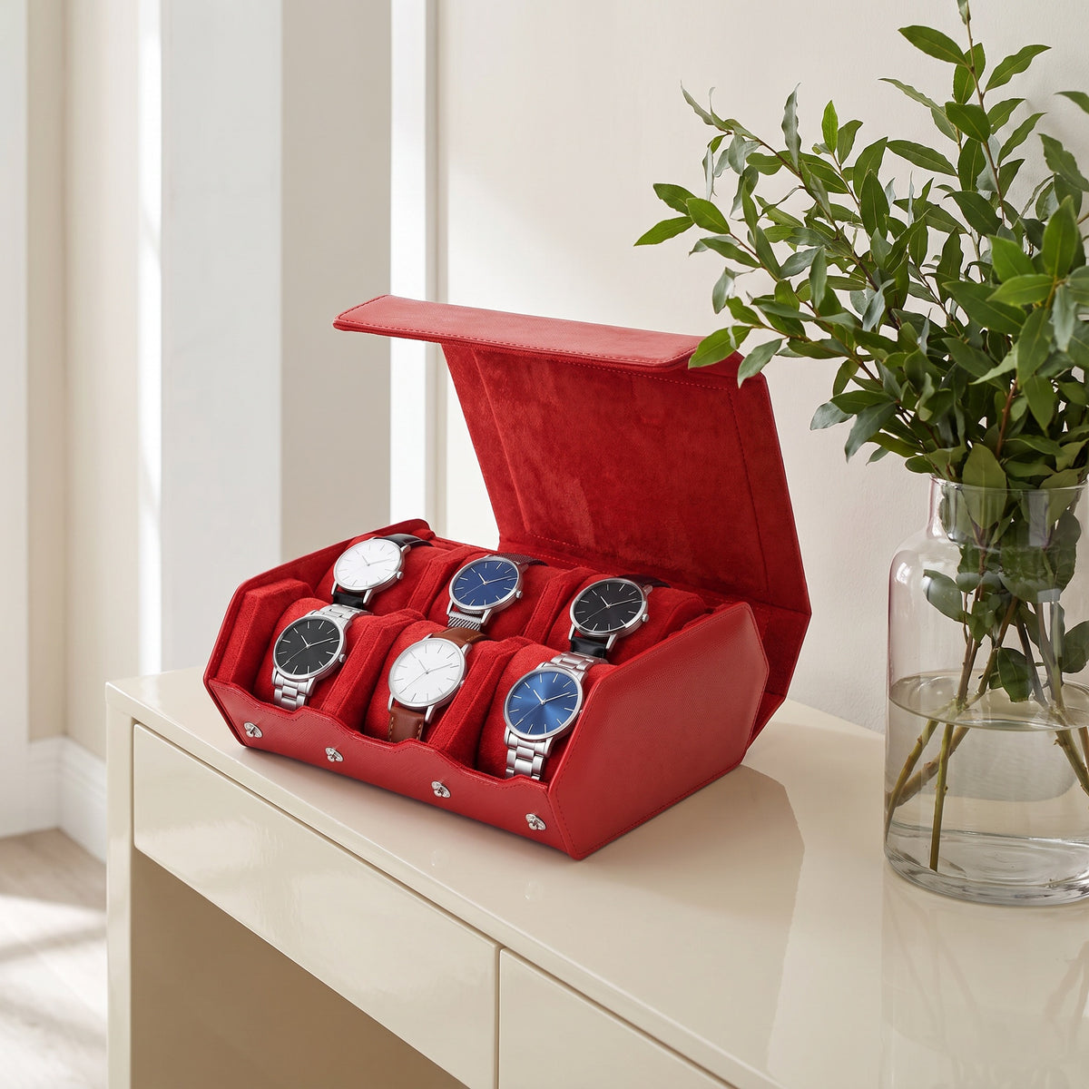 Écrin de voyage Sillage rouge 6 places ouvert et garni de montres, posé sur une console d'entrée laquée crème