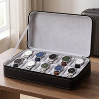 Étui de voyage pour 10 montres Voyageur noir ouvert, posé sur le bureau d'une chambre d'hôtel, valise à côté