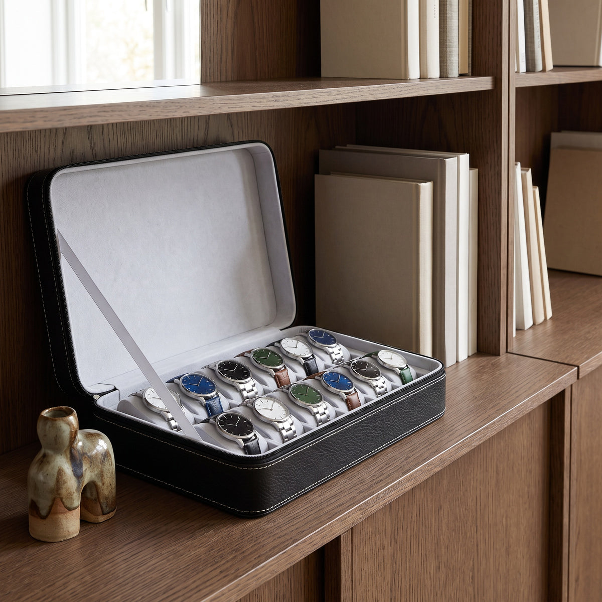 Étui de voyage pour 12 montres Voyageur noir ouvert, posé sur une étagère de bibliothèque en chêne fumé