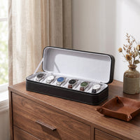 Étui de voyage pour 6 montres Voyageur noir ouvert, posé sur une commode en noyer