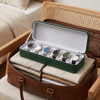 Étui de voyage pour 6 montres Voyageur vert ouvert, rangé dans un sac de voyage en cuir posé sur un fauteuil en rotin