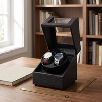 Remontoir automatique pour 2 montres Sentinelle effet carbone ouvert, posé sur un bureau en noyer devant une bibliothèque